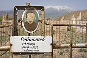 A Kyrgyz grave with photo-nameplate in a lonely graveyard, overlooked by snow-capped mountains.