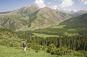 A trekker climbs through forest and green meadows to the snow-capped mountains of the Sarycat Ertas Nature Reserve.