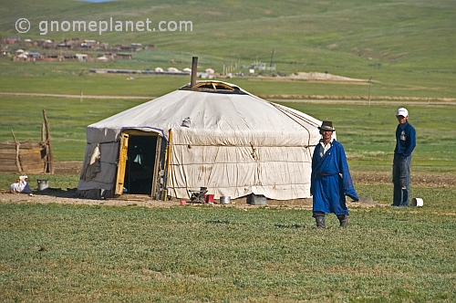 Mongolian man and boy stand next to their yurt.