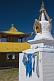 White Dagoba with blue prayer scarves and yellow wooden temple at the Singino monastery.