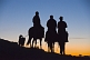 Image of Three Mongolian horsemen and dog riding into the sunset.