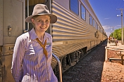 Great Southern Rail female attendant in hat next to Indian Pacific carriages.