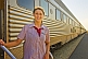 Smiling Great Southern Rail female attendant next to Ghan train carriages at Alice Springs station.