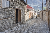 An old woman walks down the cobbled village street between houses protected from earthquake damage by wooden beams integrated in the stonework.