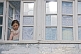 Image of A young girl in a California teeshirt looks out of the window of her village house.