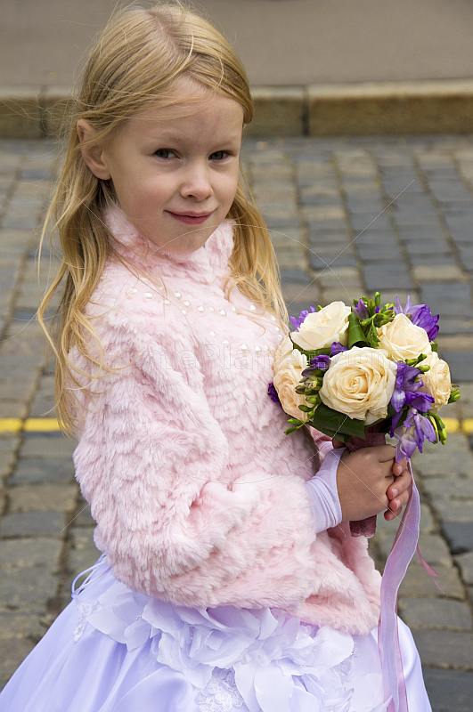 Young blonde Russian girl dressed as a bridesmaid holds a bunch of flowers on Red Square.