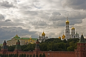 The golden domes and green copper roofs of the Kremlin contrast a cloudy sky.