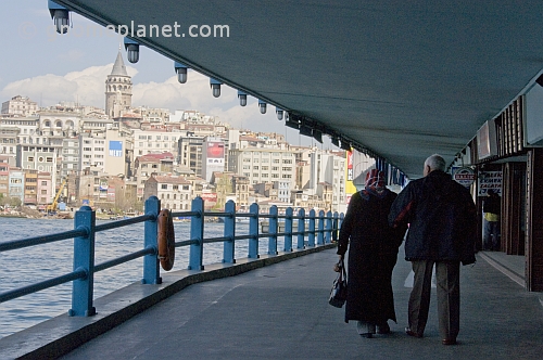 Elderly couple walk on lower deck of the Galata Bridge, to cross the Golden Horn.