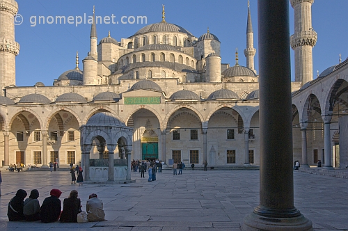 Worshippers wait in the courtyard of the Ahmet Camii Blue Mosque lit by evening sunshine.