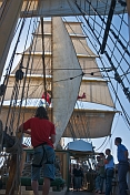 Crew stand on deck of the barque 'Picton Castle' under full sail leaving Boston harbor.