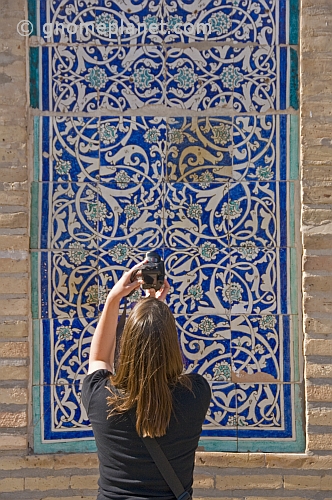 Tourist woman photographs some blue glazed ceramic tilework on the Mohammed Amin Khan Medressa.