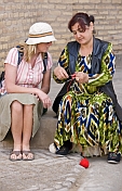 Uzbek craftswoman in Ikat dress shows a tourist some local knitting techniques.