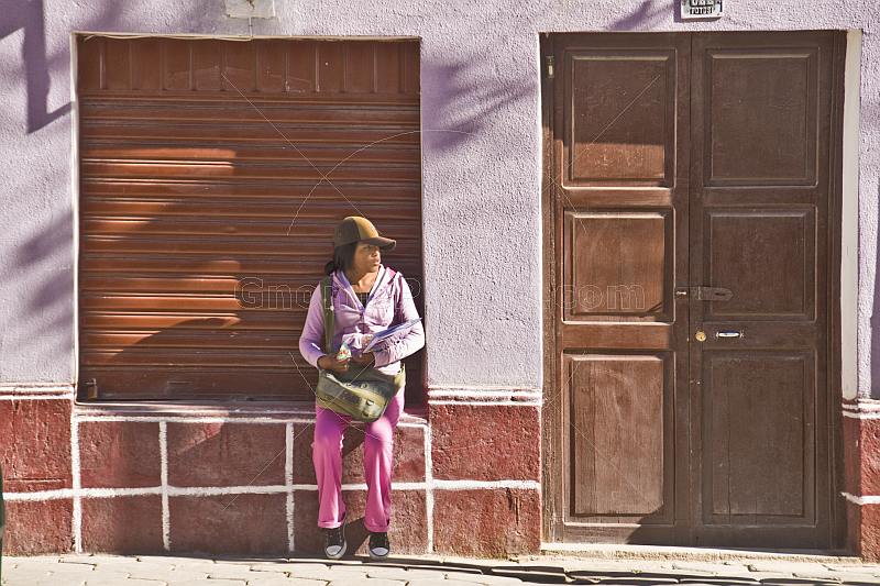 Woman in hat sits on a window cill in the Avenida Potosi.