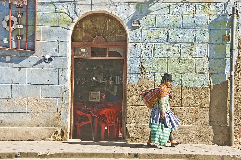 Woman in bowler hat and local dress walks past a cafe on the Avenida Potosi.