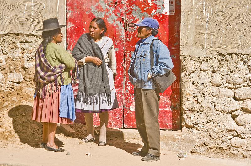 Man and two traditionally dresses Bolivian women talk outside a red door.