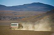 Dragoman Overland truck drives across dusty gravel valley.