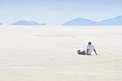 Man sits on the Uyuni Salt Flats to admire the view.