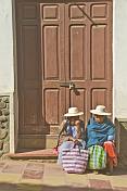 Two women with hats sit on a door step outside a locked brown door.