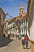 Shoppers walk along Bustillos Street with old colonial houses.