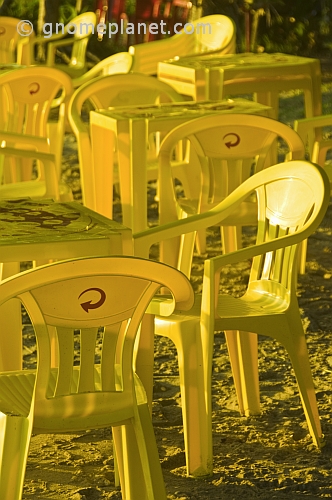 Yellow plastic chairs and tables on the beach.