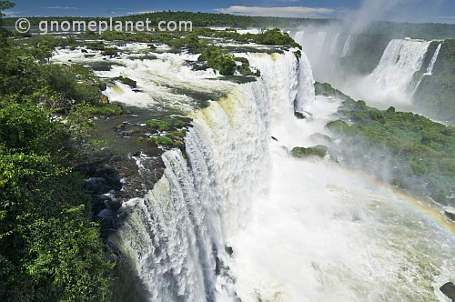 Water with rainbow cascades into the river at the Iguazu Falls.