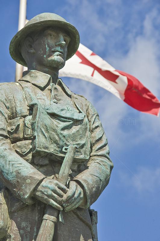 Bronze statue of Canadian soldier stands in front of National flag on memorial for World War one and two.