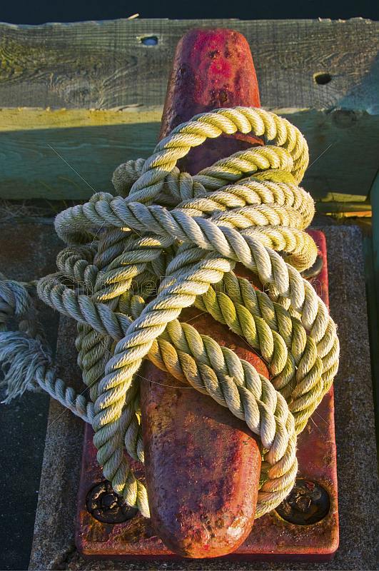 Red dock mooring bollard with white rope in early morning sunlight.