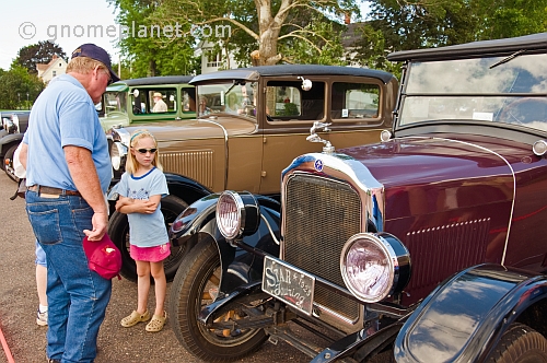 A man and a girl look at a row of vintage motor cars parked on Queens Street.