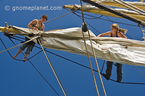 Two women crew members of the tallship 'Picton Castle' work aloft to stow sail.