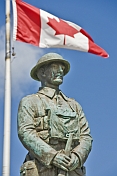 Bronze statue of Canadian soldier stands under National flag on memorial for World War one and two.