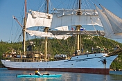 A canoeist watches the tallship 'Picton Castle' prepare to set sail and leave harbor.