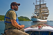 Man in small motor boat watches the square rigger \\\\'Picton Castle\\\\' as she sets sail towards the ocean.