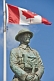 Bronze statue of Canadian soldier stands under National flag on memorial for World War one and two.