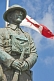 Image of Bronze statue of Canadian soldier stands in front of National flag on memorial for World War one and two.