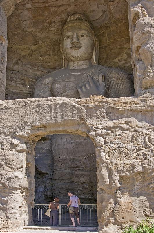 Two western tourists looking at a giant Buddha statue at the Yungang Buddhist caves, near Datong.