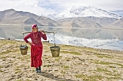 Woman carrying water from Karakul Lake, near the Karakoram Highway, with view of the snow-capped Pamir mountains.