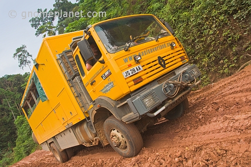 Oasis Overland truck drives through muddy section of jungle logging road.