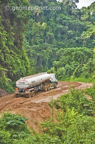 A white fuel tanker struggles to drive along muddy logging roads in the dense jungle.