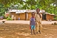 Two small brothers stand in front of their mud brick house.