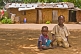 Two small brothers kneel in front of their mud brick house.