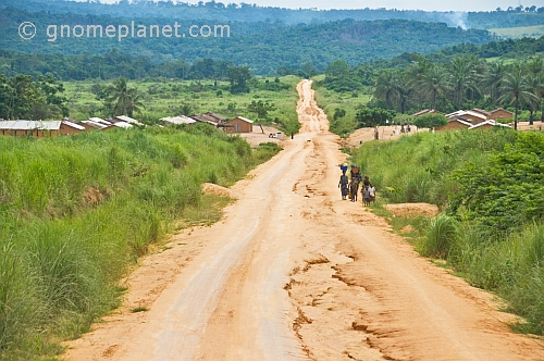 Women and children walk along the sandy main road that runs through savannah and jungle.