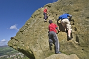 Climbers in red and blue shirts climb the Cow and Calf Rocks on Ilkley Moor.