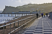 Pedestrians walk beside the sea along the esplanade in Autumn sunshine.
